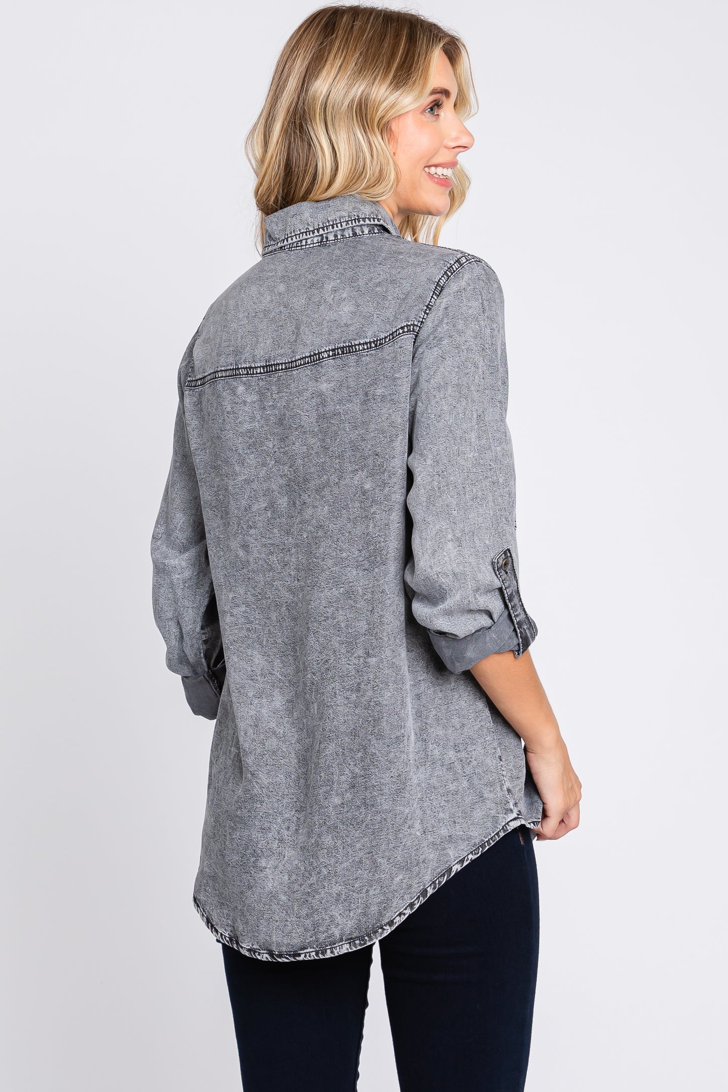 woman wearing a gray long sleeve denim shirt with rolled sleeves and curved hem, shown from the back