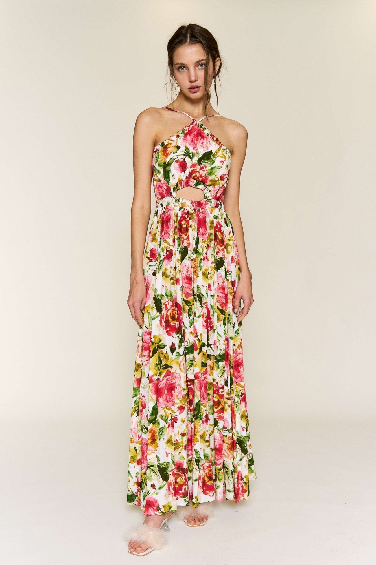 woman wearing a floral maxi dress with a halter neck and cut-out waist details, featuring vibrant pink and green colors