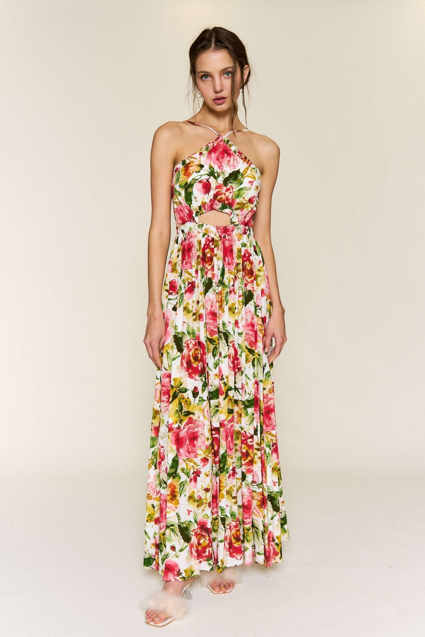 woman wearing a floral maxi dress with a halter neck and cut-out waist details, featuring vibrant pink and green colors