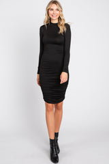 woman wearing a fitted black long sleeve dress with ruching on the sides and black ankle boots