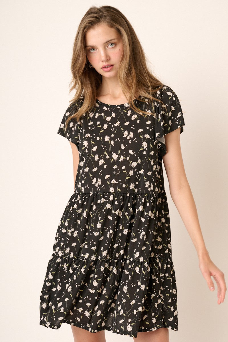 woman wearing a black short sleeve tiered mini dress with white daisy floral print
