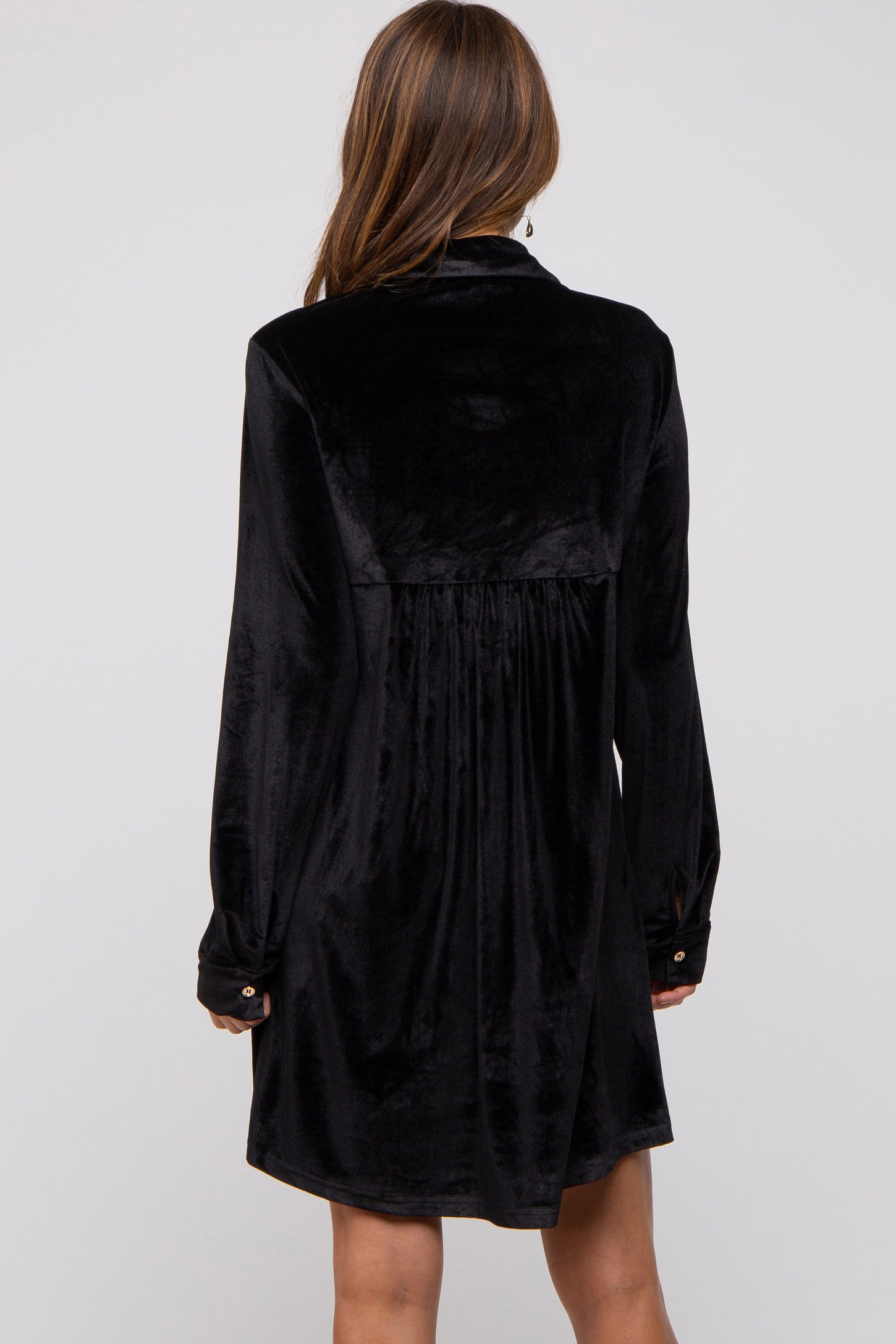 woman wearing a black velvet long sleeve dress with a pleated back and buttoned cuffs, shown from the back