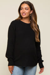 woman wearing a black maternity sweater with a textured knit design and holding her baby bump