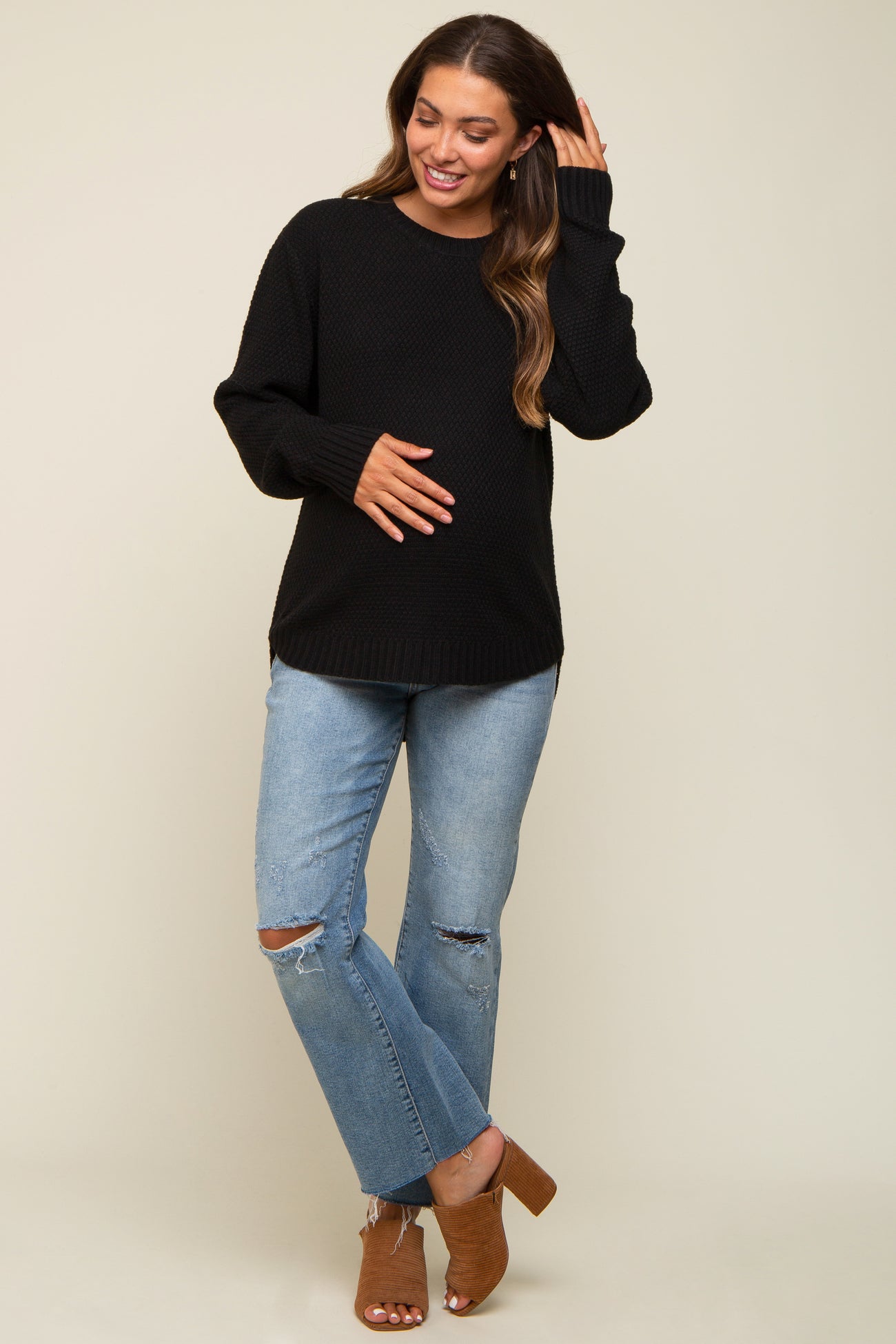 woman wearing a black maternity sweater and distressed jeans, smiling and holding her baby bump