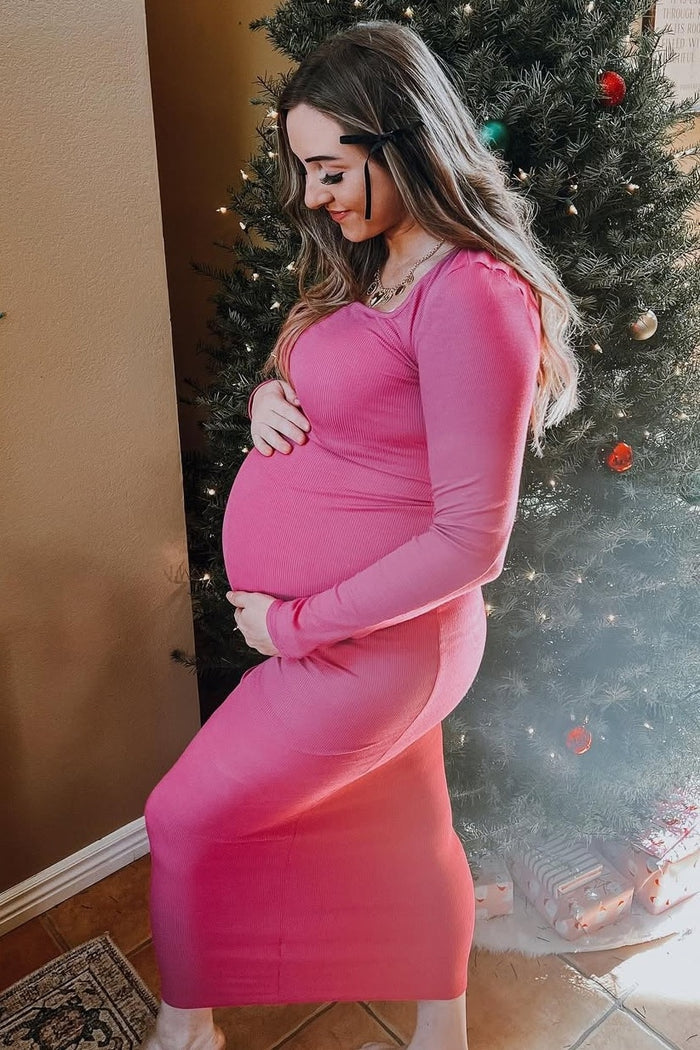 woman wearing a hot pink ribbed maternity dress showcasing her baby bump in front of a decorated Christmas tree