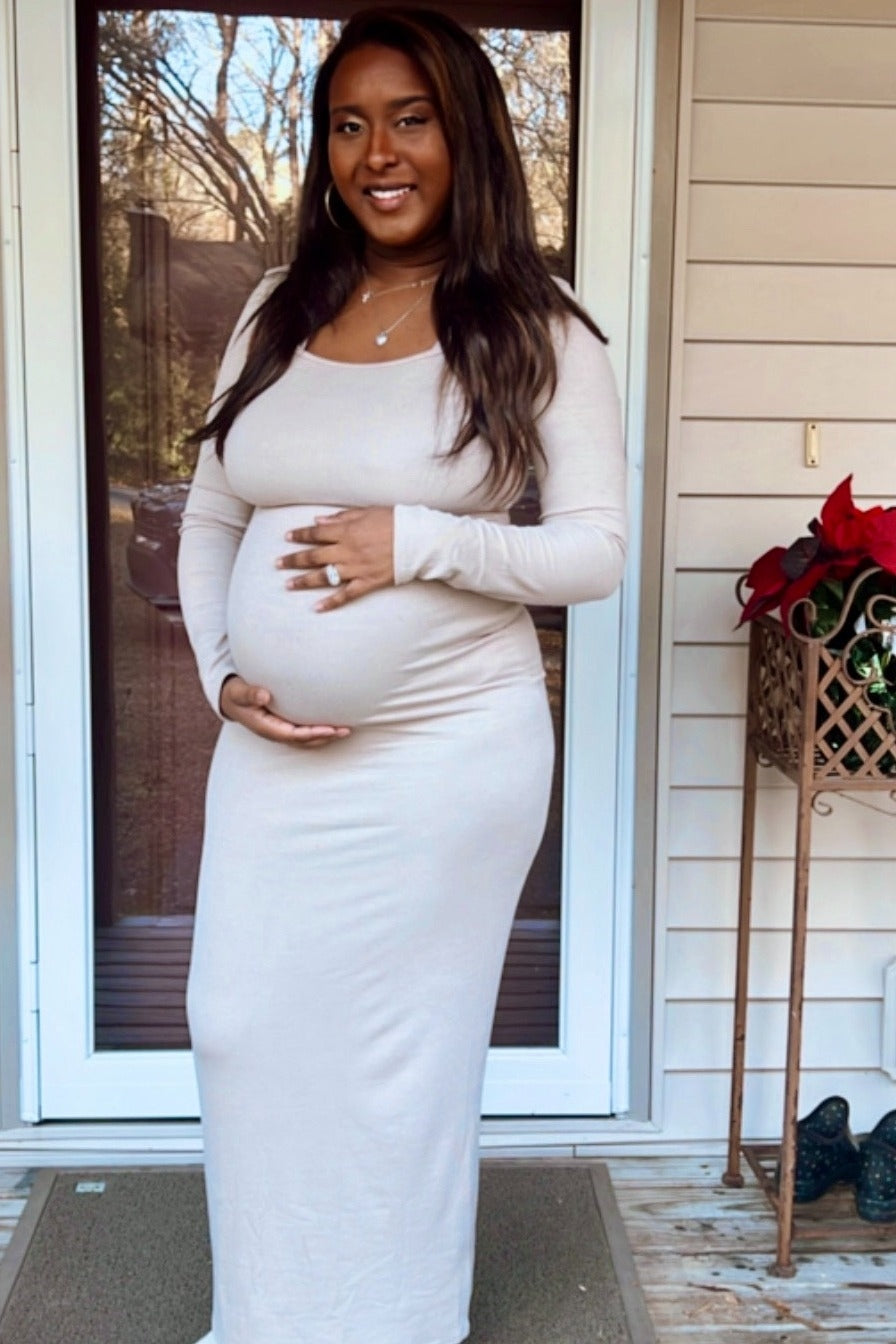 woman wearing a light beige long sleeve maternity dress and holding her baby bump