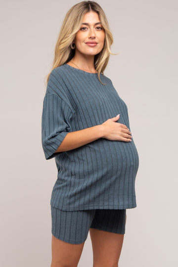 woman wearing a blue ribbed maternity two-piece set, standing with a visible baby bump and hands on her stomach