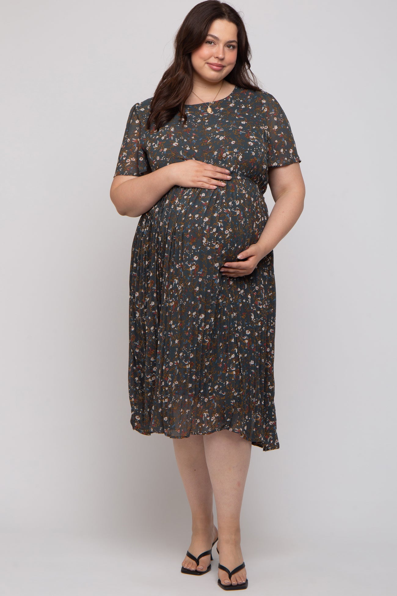 woman wearing a floral pattern short sleeve maternity dress and gently holding her baby bump
