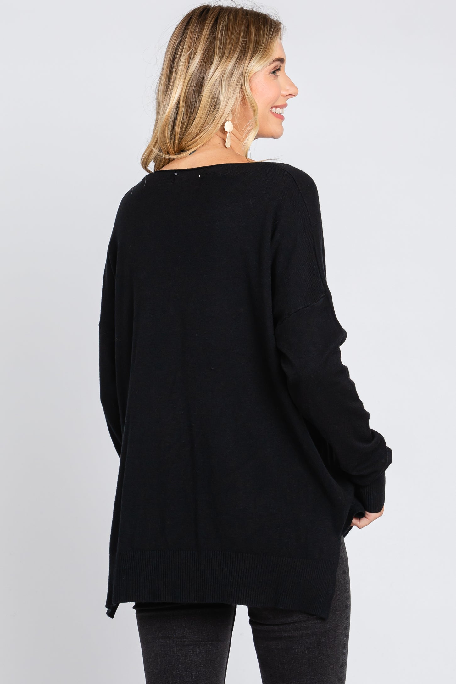 woman wearing a black oversized sweater with a relaxed fit and a rounded hem, shown from the back