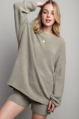 woman wearing an oversized light gray textured sweater with matching shorts and a gold pendant necklace