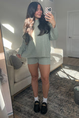 woman wearing a light green oversized sweater and matching shorts, posing in front of a mirror with a casual outfit