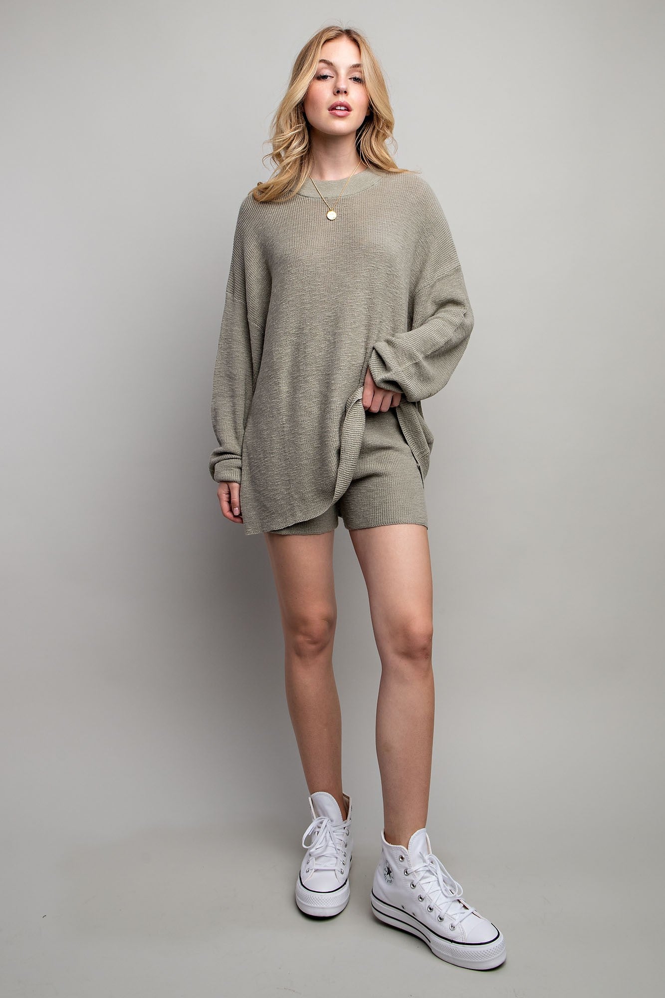 woman wearing a light olive green oversized sweater and matching shorts with white sneakers