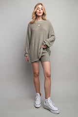 woman wearing a light olive green oversized sweater and matching shorts with white sneakers