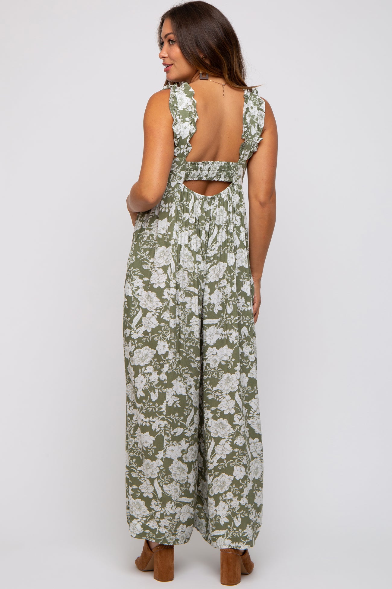 woman wearing a floral patterned olive green maternity jumpsuit with ruffle straps and an open back