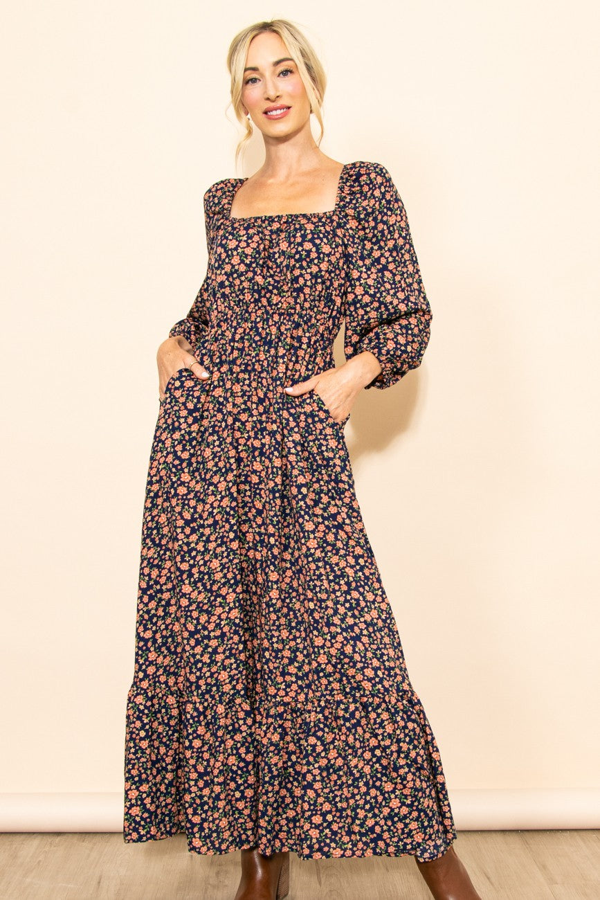 woman wearing a navy blue floral maxi dress with long sleeves and pockets, standing with hands in pockets