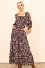 woman wearing a navy blue floral maxi dress with long sleeves and pockets, standing with hands in pockets