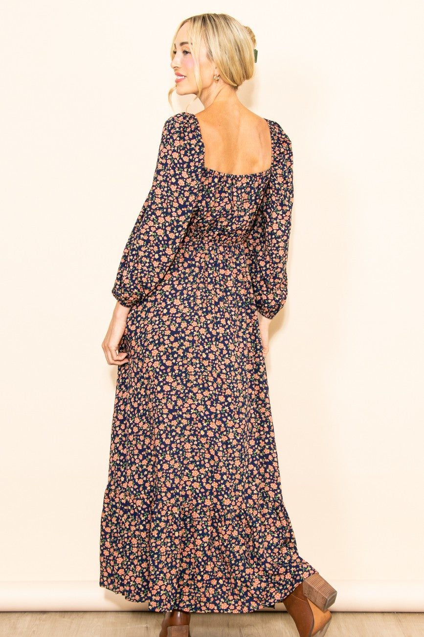 woman wearing a floral navy blue maxi dress with long sleeves and a square back, standing sideways to the camera