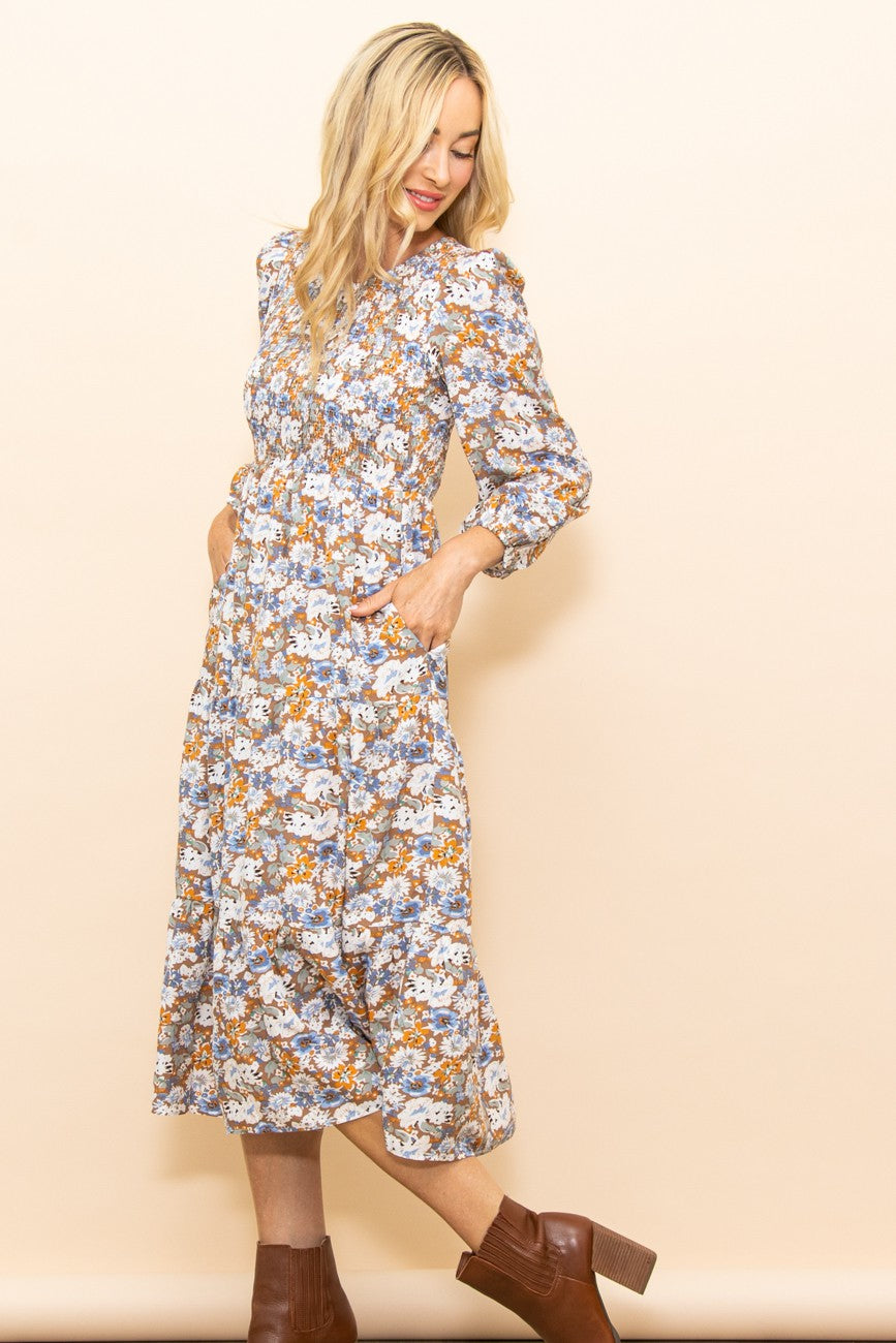 woman wearing a floral midi dress with long sleeves and pockets, styled with brown chunky heeled boots