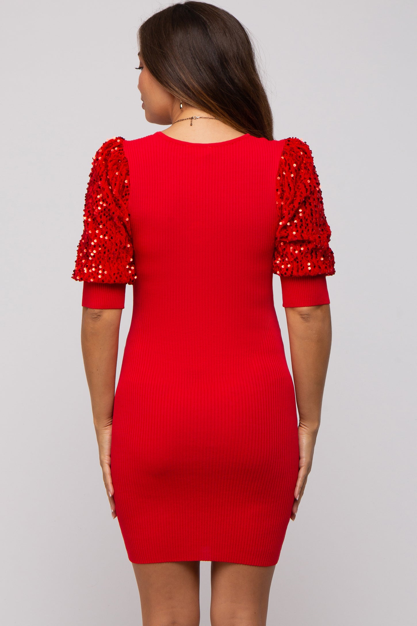woman wearing a red maternity dress with sequin-embellished puff sleeves and a fitted silhouette