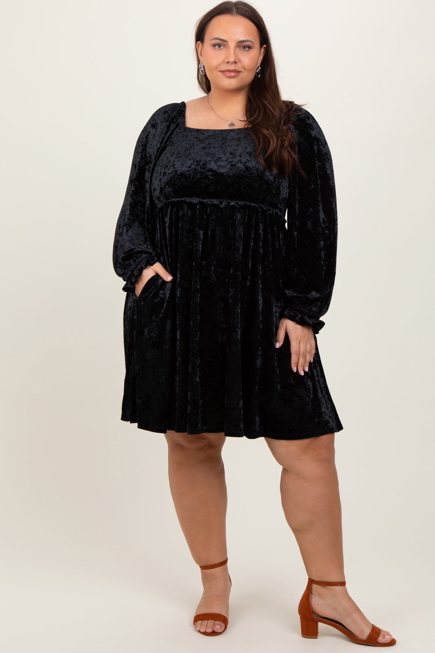 woman wearing a black velvet plus-size dress with long sleeves and pockets, standing in a relaxed pose