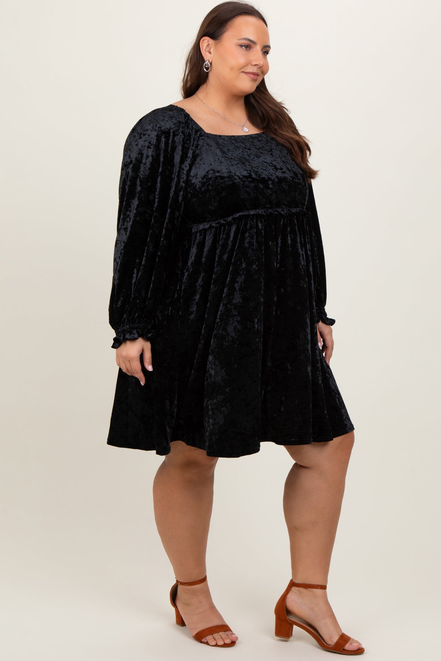 woman wearing a black velvet plus size dress with long sleeves and a relaxed fit, paired with strappy brown heels