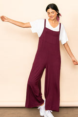 woman wearing a burgundy jumpsuit with wide legs over a white t-shirt, smiling and posing against a beige background