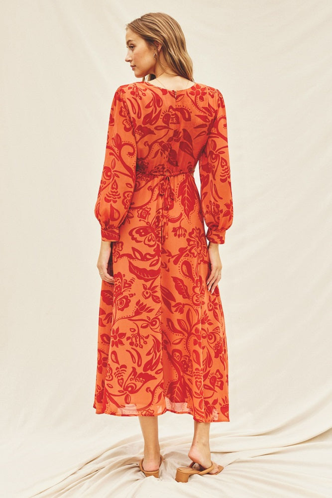 woman wearing a red floral print midi dress with long sleeves and a cinched waist, viewed from the back