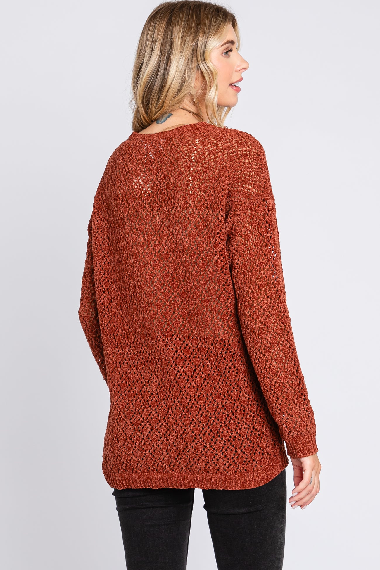 woman wearing a rust-colored open knit sweater with long sleeves and a relaxed fit, viewed from the back