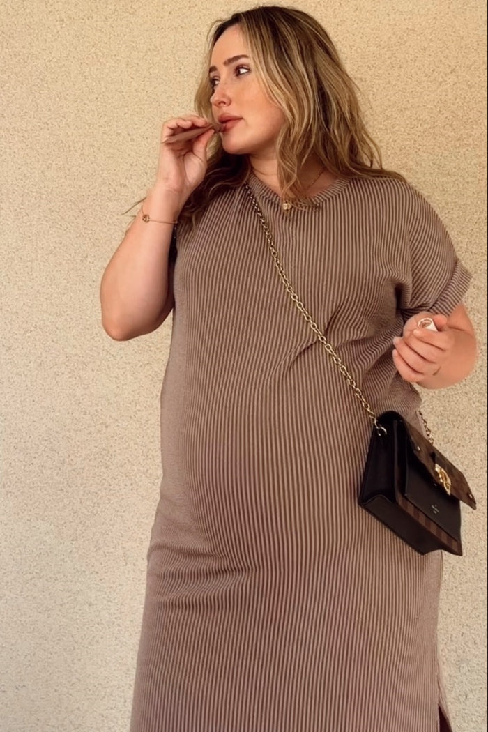 woman wearing a brown striped maternity dress with short sleeves and a baby bump, holding a small handbag