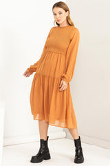 woman wearing an orange long sleeve midi dress with a smocked bodice and tiered skirt, paired with black ankle boots