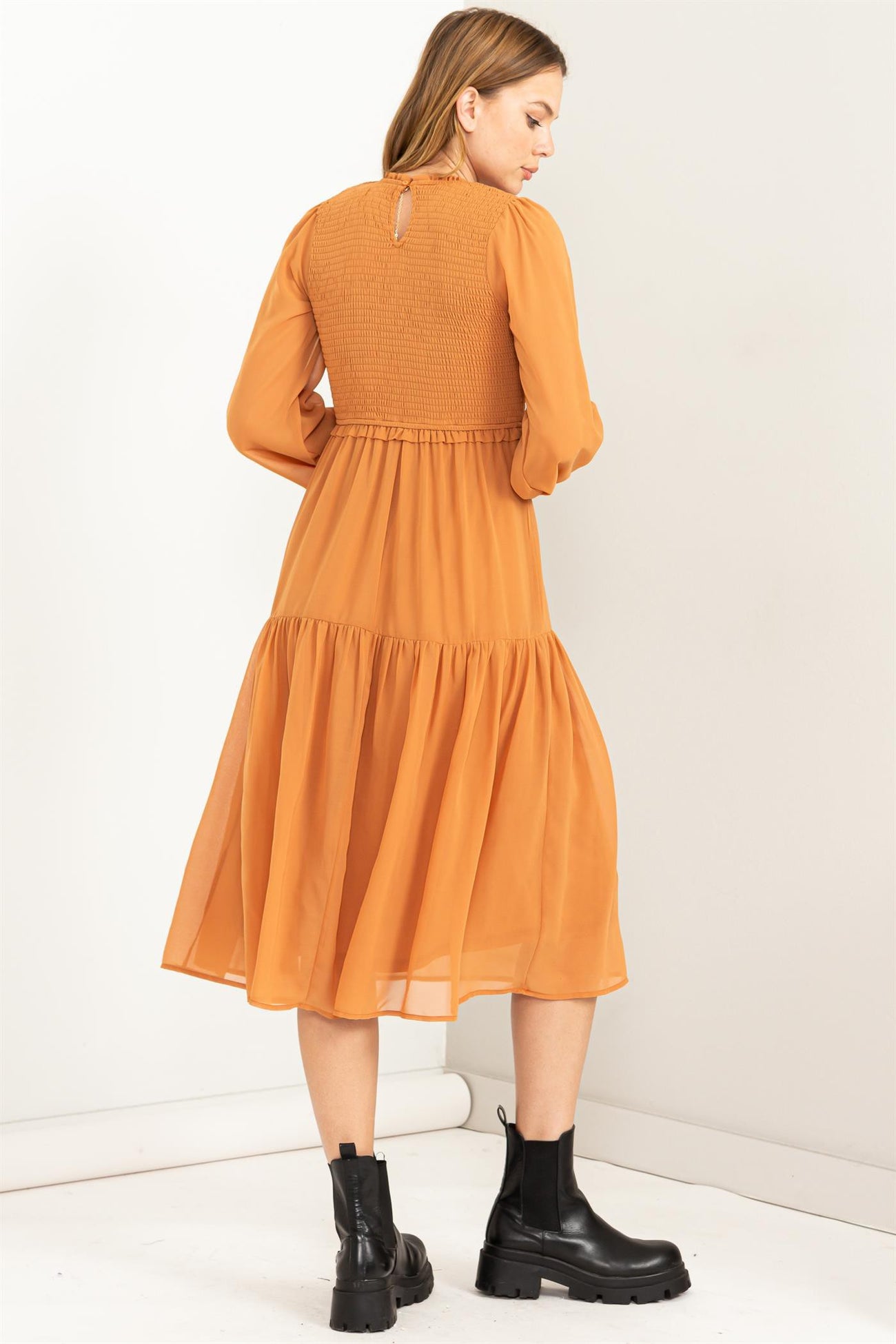 woman wearing an orange long sleeve dress with a smocked bodice and tiered skirt, viewed from the back