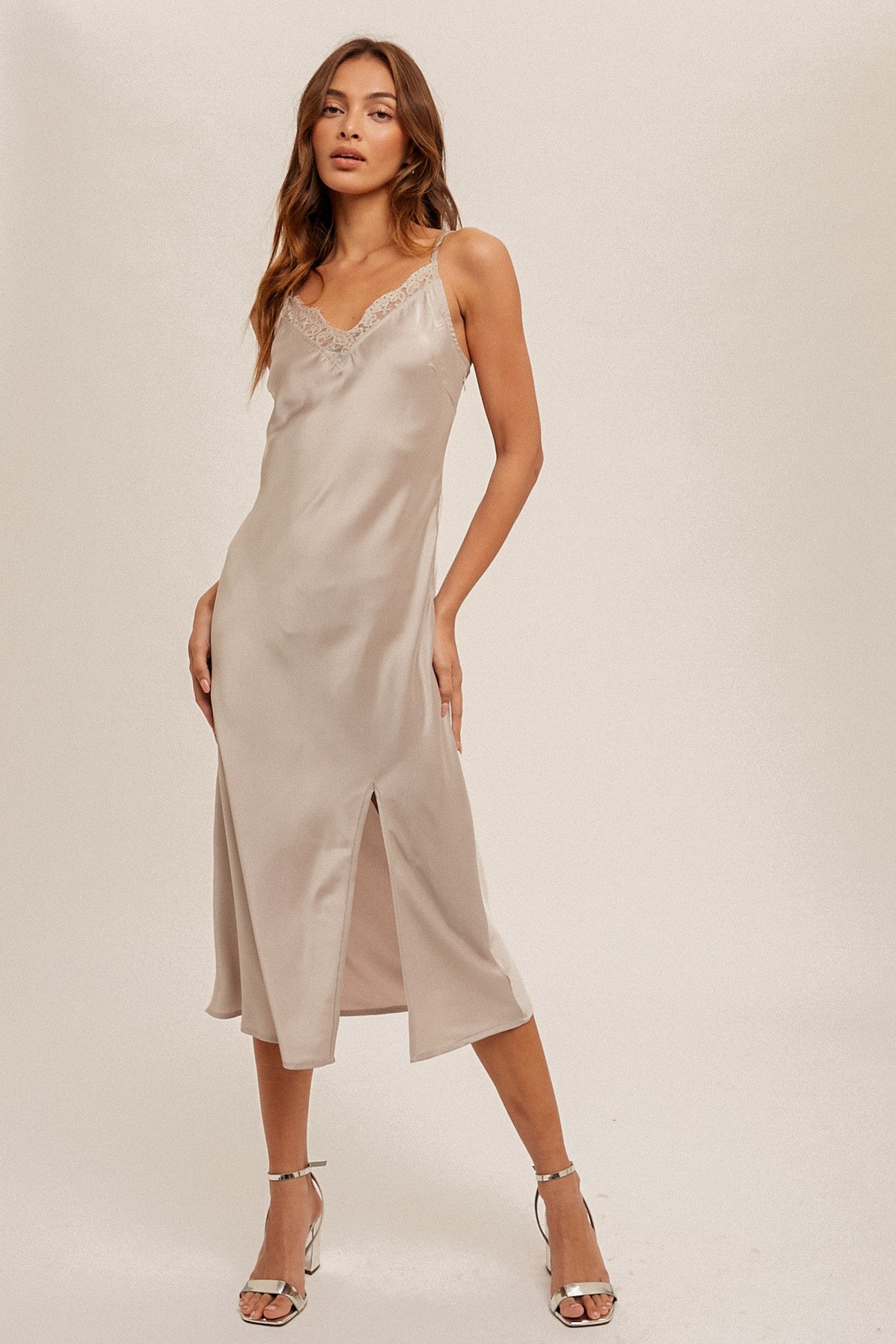 woman wearing a beige satin slip dress with lace trim and side slits, standing in a stylish pose