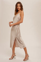 woman wearing a beige satin midi dress with a side slit and thin spaghetti straps, styled with silver high heels