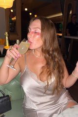 woman wearing a light silver satin slip dress and sipping a cocktail in a stylish setting
