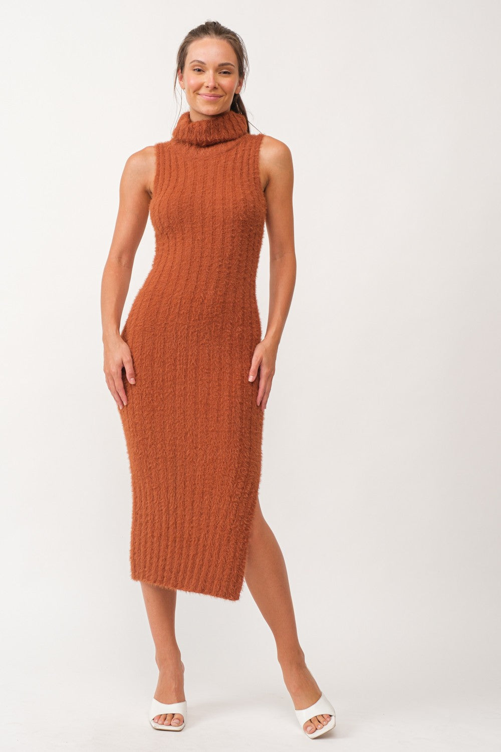 woman in a rust-colored knit midi dress with a mock neck and side slit, wearing white heeled sandals
