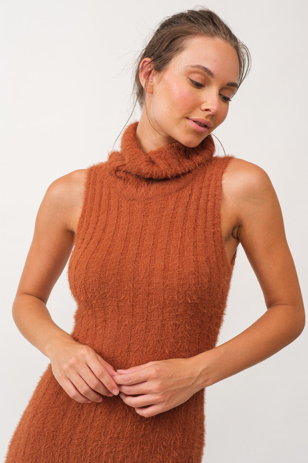 woman wearing a rust-colored sleeveless turtleneck sweater dress with a ribbed texture