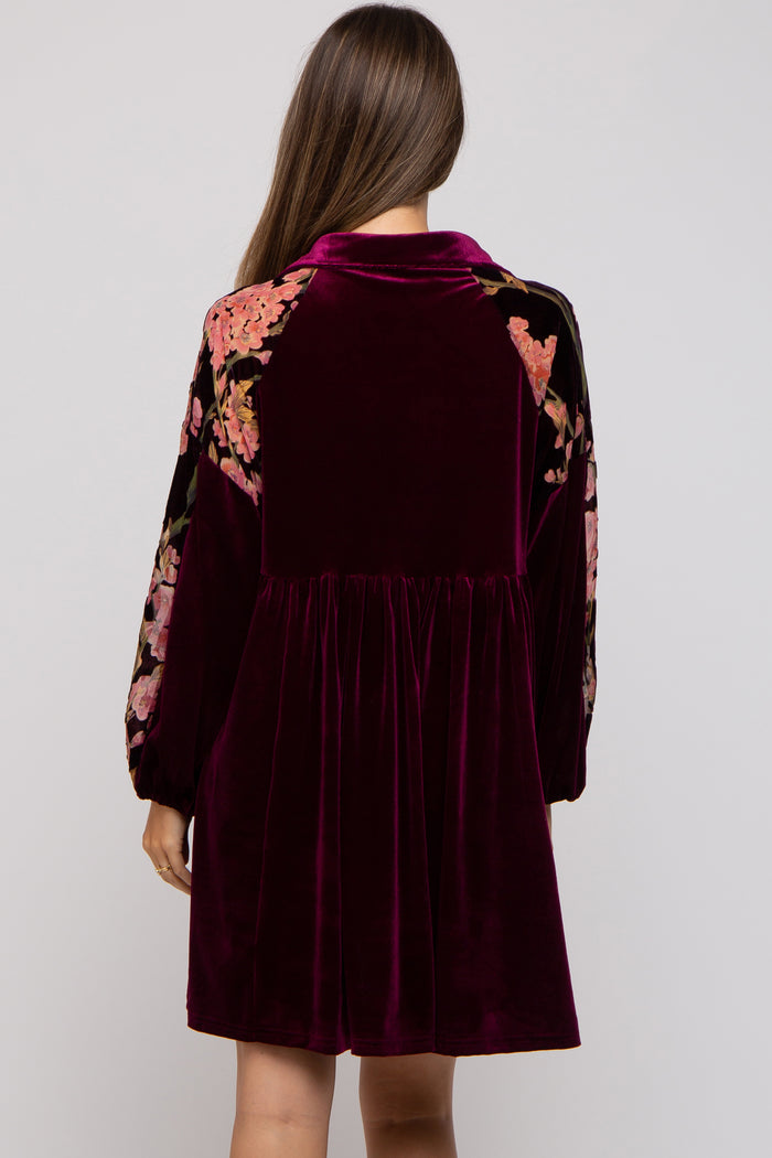 woman wearing a burgundy velvet maternity dress with floral embroidered details on the shoulders and long sleeves