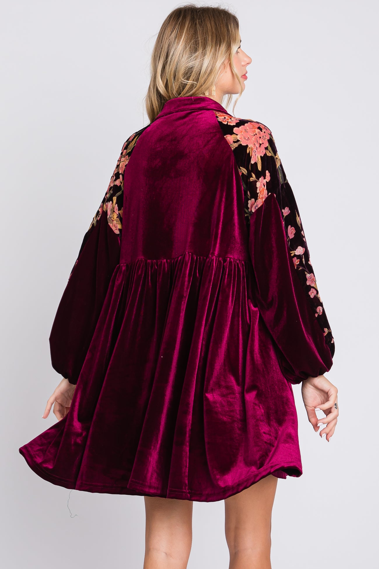 woman wearing a rich burgundy velvet dress with floral embroidery on the shoulders and a flared silhouette