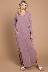woman wearing a mauve long sleeve maxi dress with side slits and pockets, standing on a beige background