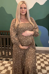 woman wearing a brown floral maternity dress, holding her baby bump while standing in a nursery setting