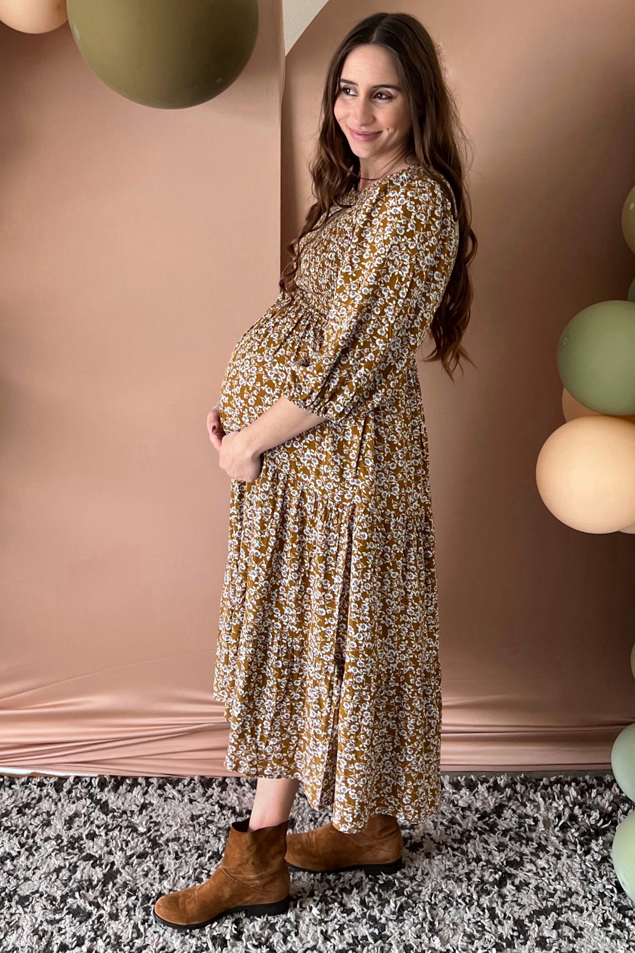 woman wearing a long sleeve mustard floral maternity dress and showcasing her baby bump