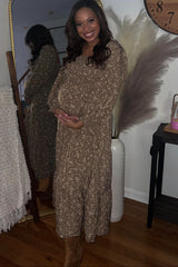 woman wearing a taupe floral print maternity maxi dress with a baby bump and smiling in front of a mirror