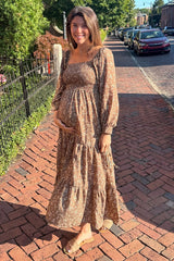 woman wearing a brown floral maternity dress with long sleeves and a tiered skirt, holding her baby bump