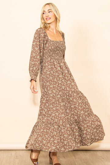 woman wearing a brown floral maxi dress with a square neckline and long sleeves, smiling against a beige background