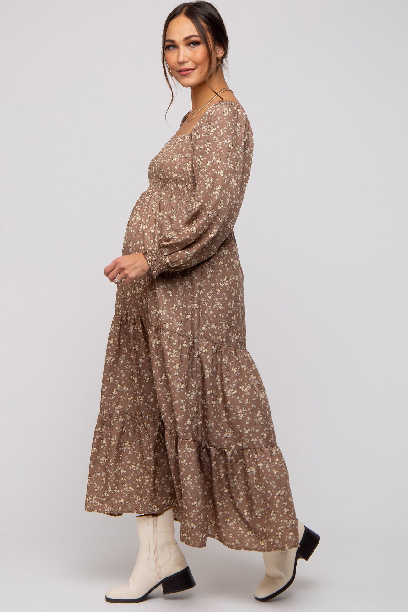 woman wearing a brown floral maternity maxi dress with a tiered skirt and long sleeves, showing her baby bump