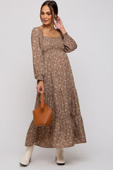 woman wearing a brown floral maternity maxi dress with long sleeves and a baby bump, holding a brown handbag