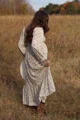 woman wearing a floral long sleeve maxi dress and holding the fabric while walking in a field