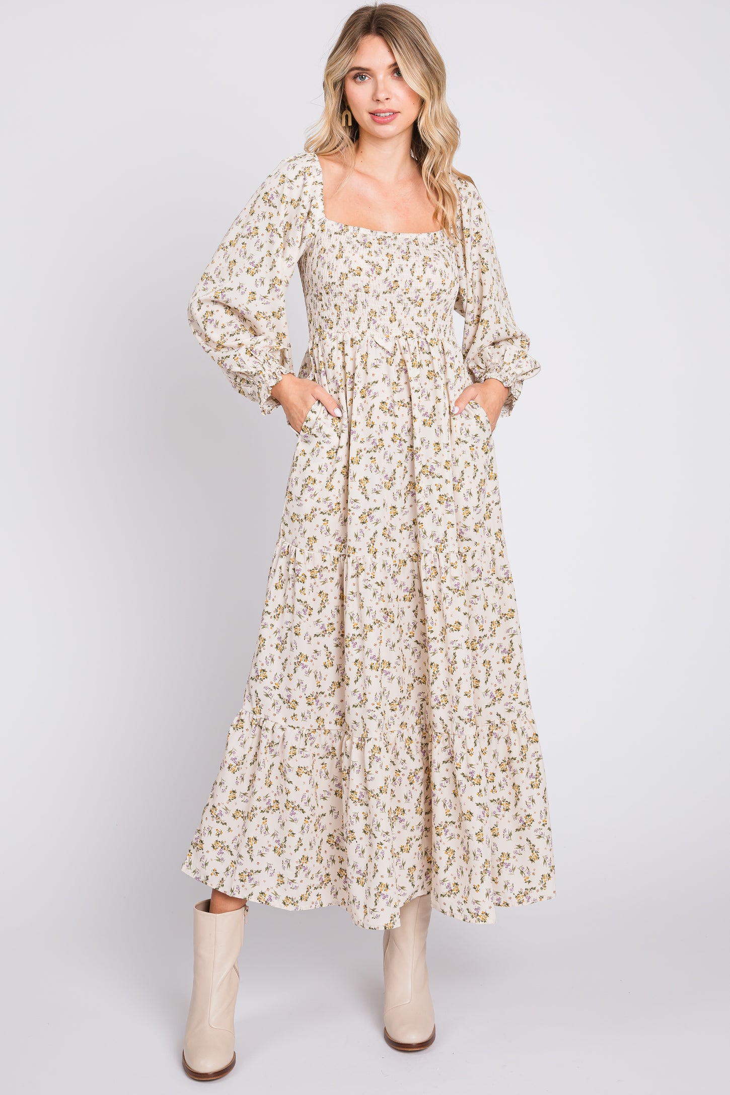 woman wearing a cream floral maxi dress with long sleeves and pockets, styled with beige ankle boots