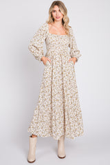 woman wearing a cream floral maxi dress with long sleeves and pockets, styled with beige ankle boots