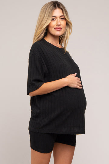 woman wearing a black ribbed maternity top and shorts, holding her baby bump